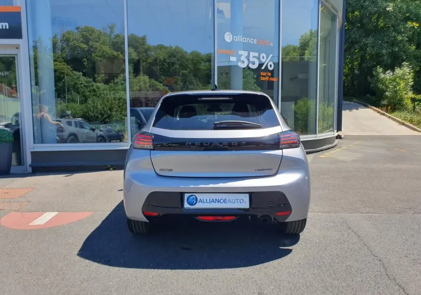 Vue arrière d'une Peugeot 208 hybride gris Artense stationnée devant une vitrine avec logo Alliance Auto.