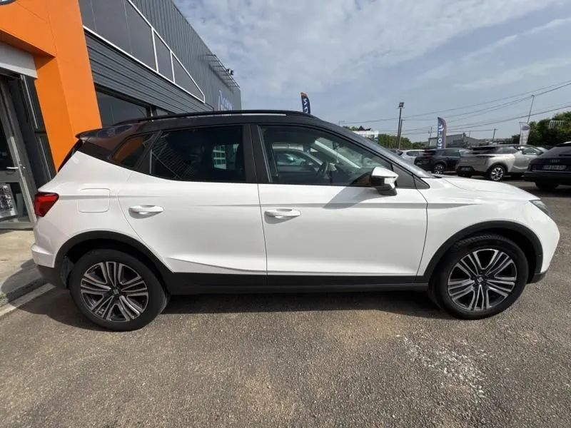 Profil côté gauche d'un SEAT Arona blanc Nevada avec toit gris magnétique, jantes alliage 17 pouces, garé en extérieur.