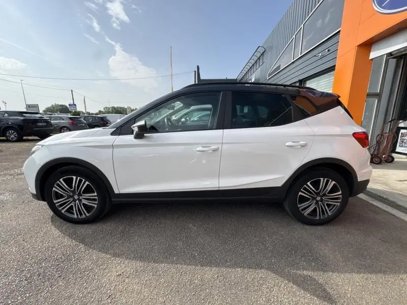 Vue latérale droite d'un SEAT Arona blanc Nevada avec toit gris magnétique, jantes alliage 17 pouces et protections noires.