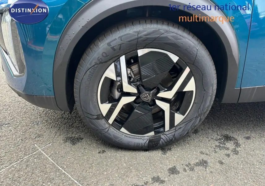 Gros plan sur la roue avant gauche du Peugeot 2008 Hybrid 136ch en bleu Obsession Metal avec jante noire et argentée.