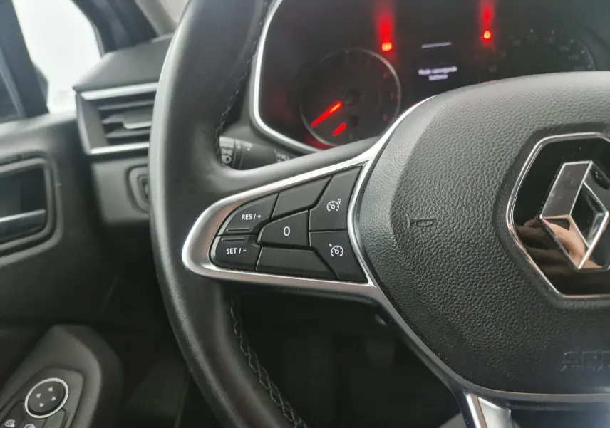 Gros plan sur le volant noir de la Renault Clio V 1.0 TCE 90 Zen avec commandes de régulateur de vitesse et tableau de bord éclairé.