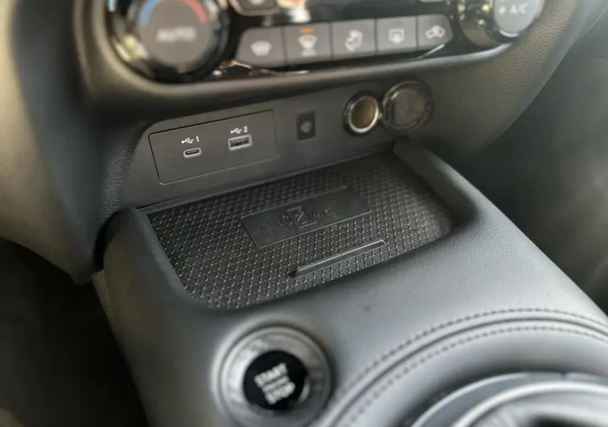 Gros plan sur la console centrale du Nissan Juke 2025 noir, montrant le bouton Start/Stop et les ports USB.