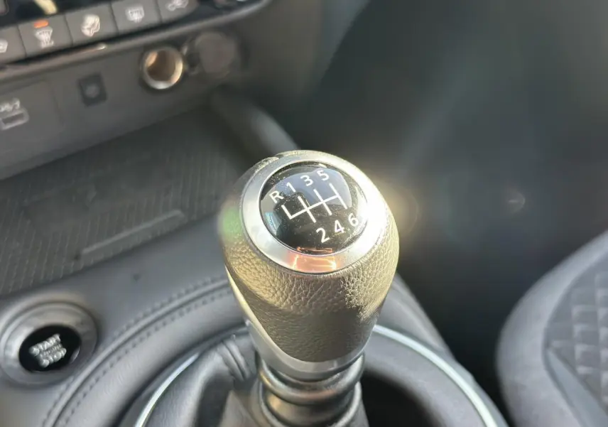 Gros plan sur le levier de vitesses manuel noir du Nissan Juke 2025, avec console et siège partiellement visibles.