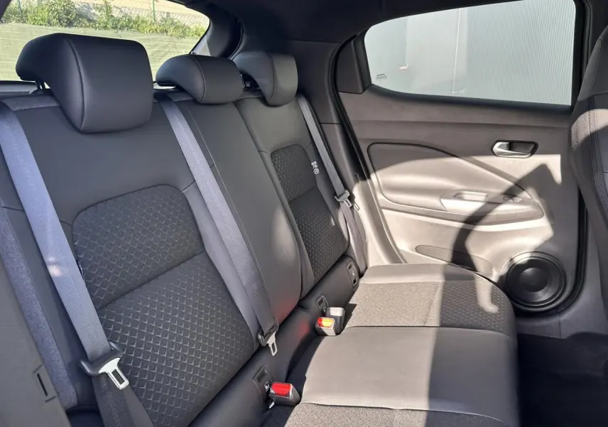 Vue latérale droite de la banquette arrière noire du Nissan Juke 2025 avec ceintures de sécurité et haut-parleur intégré.