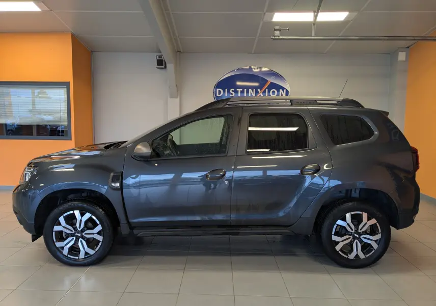 Vue de profil côté gauche du Dacia Duster gris 2023 avec jantes alliage bicolores et toit noir en showroom.