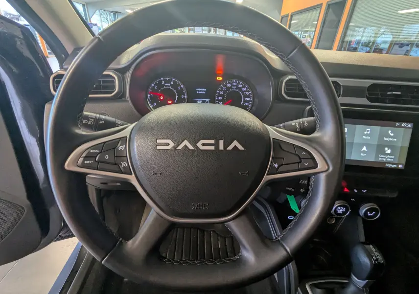 Vue intérieure centrée sur le volant noir du Dacia Duster 2023 avec tableau de bord et écran tactile visibles.