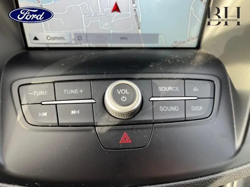 Gros plan sur les commandes audio centrales du tableau de bord du Ford C-MAX gris lunaire, avec écran GPS en arrière-plan.