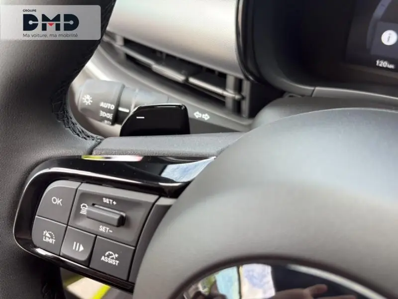 Gros plan sur les commandes au volant noir de la FIAT 600 hybride, avec tableau de bord et écran partiellement visibles.