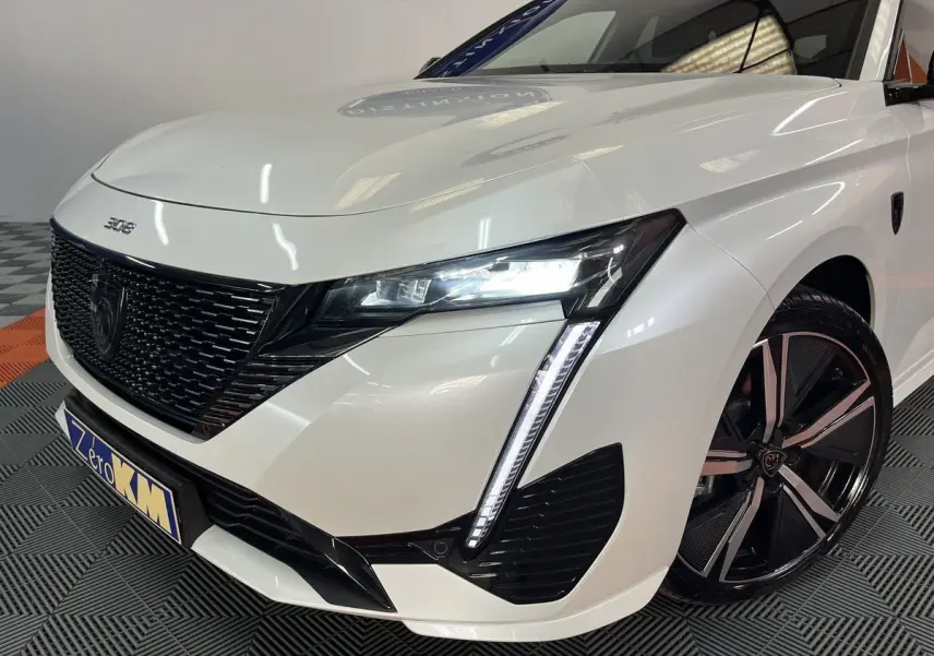 Vue 3/4 avant droit d'une Peugeot 308 GT PHEV blanche nacrée avec phares LED et jantes alliage noires.