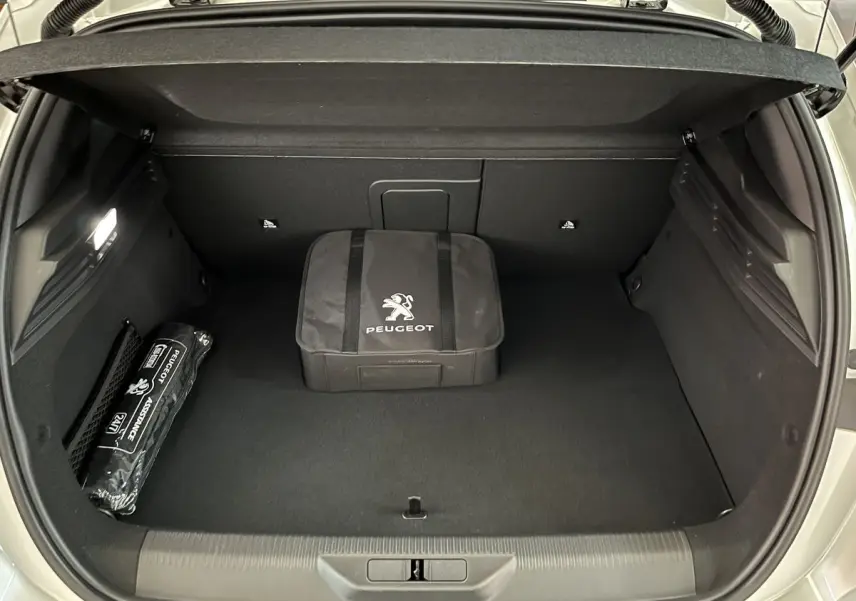 Coffre ouvert d'une Peugeot 308 GT PHEV blanc nacré, montrant un sac Peugeot et un kit d'assistance rangés.