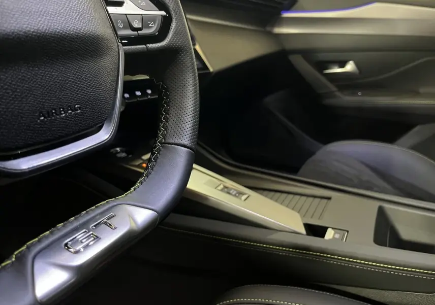 Gros plan sur le volant GT et la console centrale noire avec surpiqûres vertes d'une Peugeot 308 GT PHEV 2022.