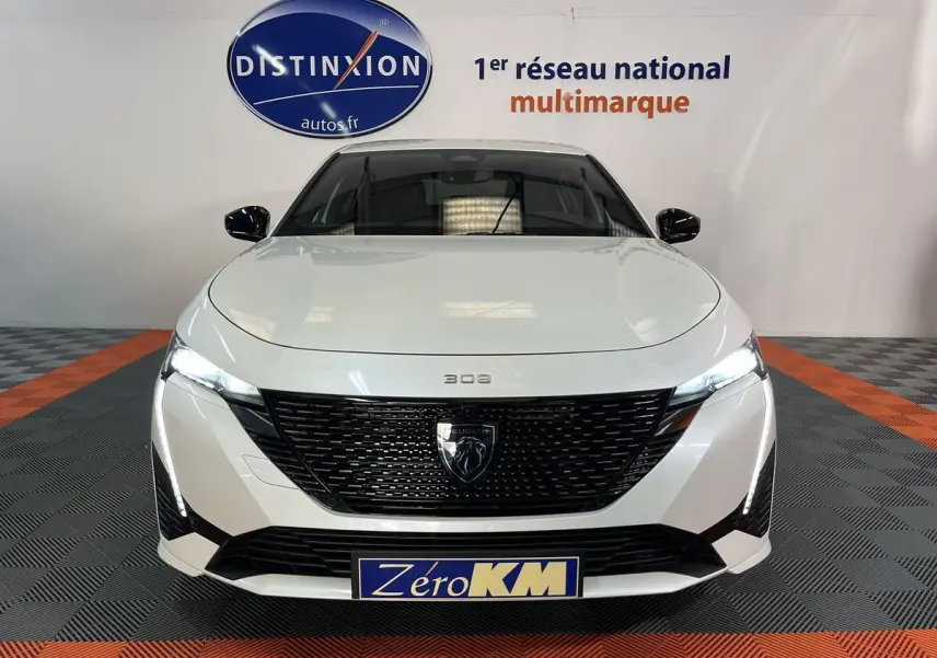 Vue frontale d'une Peugeot 308 GT PHEV blanche nacrée avec calandre noire et phares LED allumés.