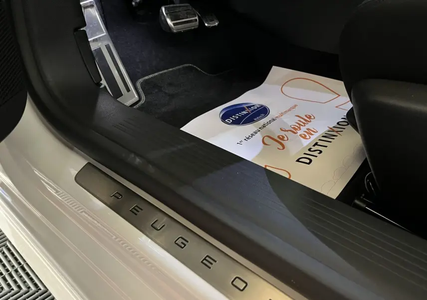 Gros plan sur le seuil de porte côté conducteur blanc nacré d'une Peugeot 308 GT PHEV 2022 avec pédales sport en aluminium.