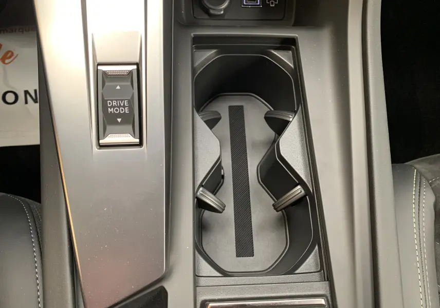 Gros plan sur la console centrale noire avec porte-gobelets et bouton Drive Mode de la Peugeot 308 GT PHEV blanc nacré.