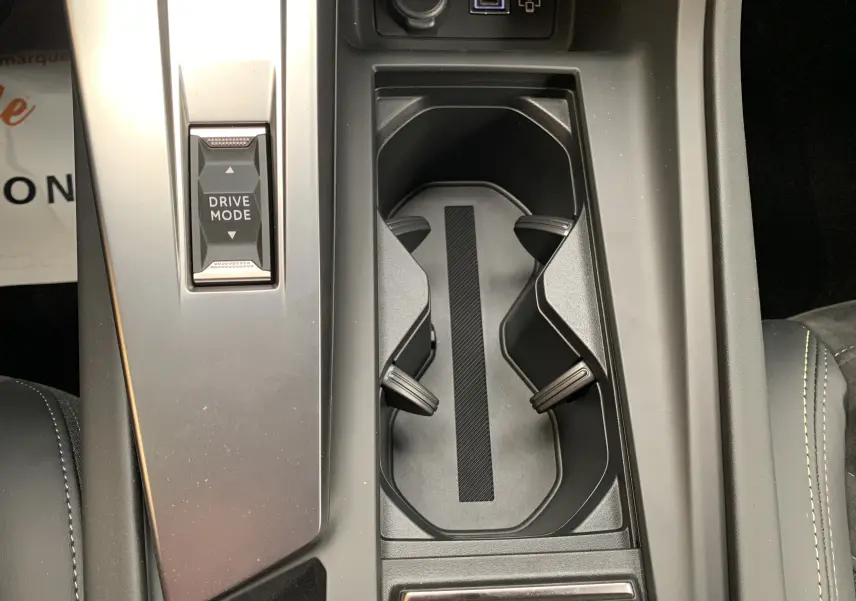 Vue rapprochée de la console centrale noire de la Peugeot 308 GT PHEV avec bouton Drive Mode et porte-gobelets.