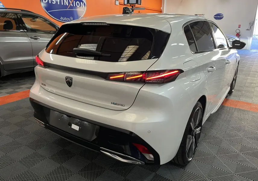 Vue 3/4 arrière droite d'une Peugeot 308 GT PHEV blanche nacrée avec feux LED allumés dans un showroom.
