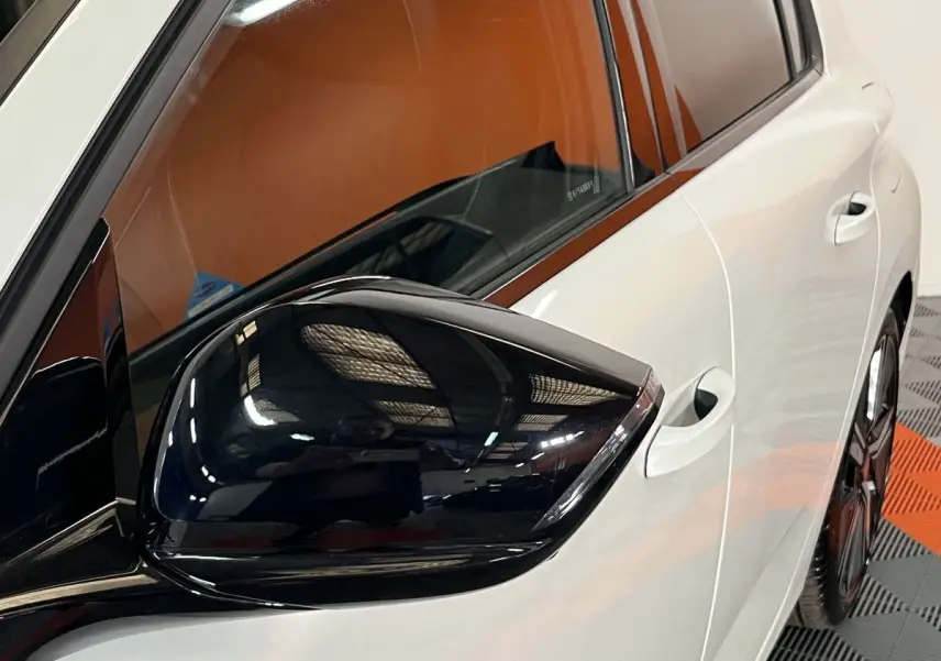 Vue rapprochée du rétroviseur noir côté gauche sur la porte blanche nacrée d’une Peugeot 308 GT PHEV 2022.