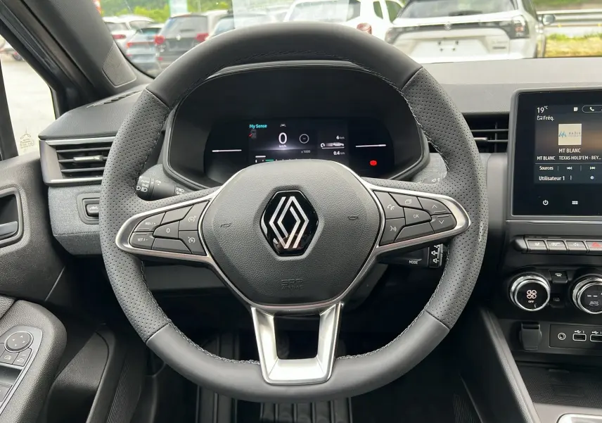 Vue centrée sur le volant perforé de la Renault Clio V TCE 90 Techno 2025 avec tableau de bord numérique et écran tactile.