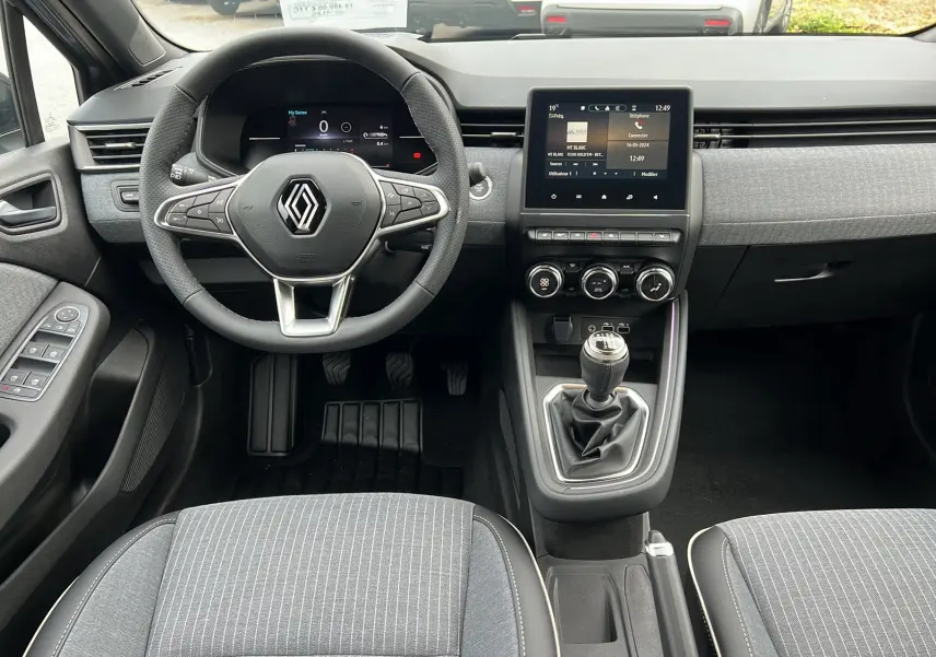 Vue intérieure avant de la Renault Clio V TCE 90 Techno 2025 avec tableau de bord moderne et levier de vitesse manuel.