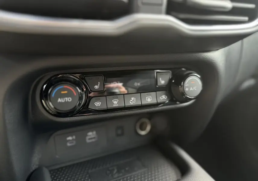 Gros plan sur la console centrale du Nissan Juke blanc nacré 2025, mettant en valeur les commandes de climatisation automatique et sièges chauffants.