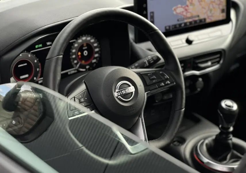 Vue rapprochée de l'intérieur du Nissan Juke 2025 montrant le volant cuir, la boîte manuelle et l'écran tactile central.