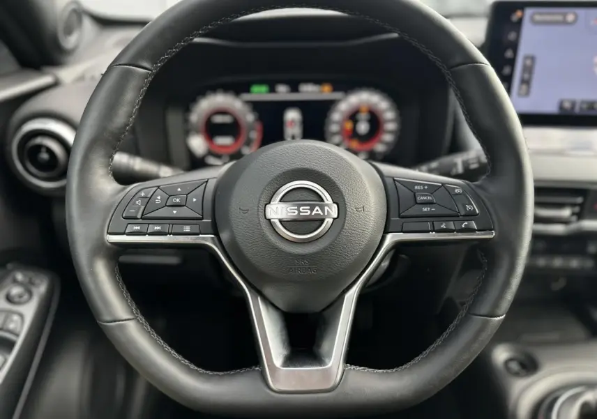 Volant en cuir noir de Nissan Juke 2025 avec commandes intégrées et tableau de bord digital en arrière-plan.