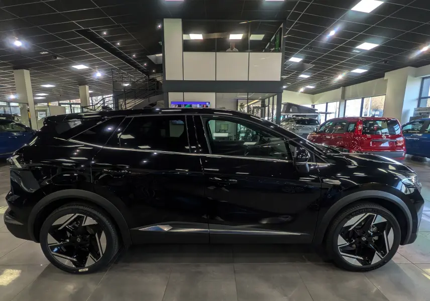 Profil côté gauche du Renault SYMBIOZ E-Tech full hybrid noir étoilé, soulignant ses jantes noires et détails chromés en intérieur showroom.