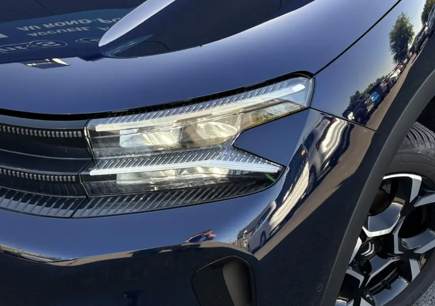 Gros plan sur l'avant droit bleu Eclipse du Citroën C5 Aircross 2025, mettant en valeur le phare LED et la jante alliage bi-ton.