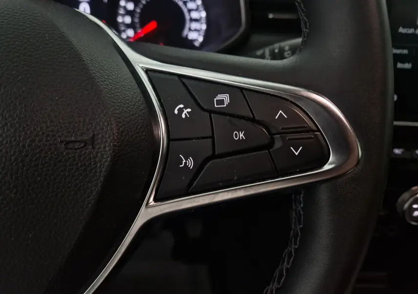 Gros plan sur les commandes multimédias à droite du volant noir de la Renault Clio V gris platine, tableau de bord en arrière-plan.