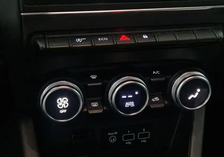 Gros plan sur les commandes de climatisation et boutons de fonction d'une Renault Clio V gris platine, intérieur sombre.