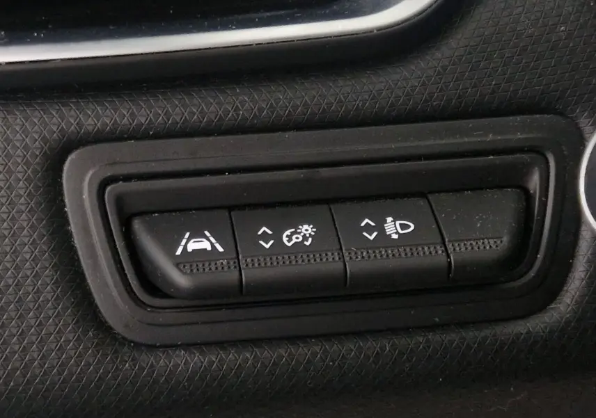 Gros plan sur les boutons de réglage d'assistance et d'éclairage du tableau de bord d'une Renault Clio V gris platine.