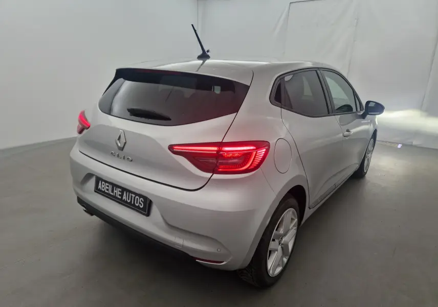 Vue 3/4 arrière droite d'une Renault Clio V gris platine avec feux arrière allumés dans un studio blanc.