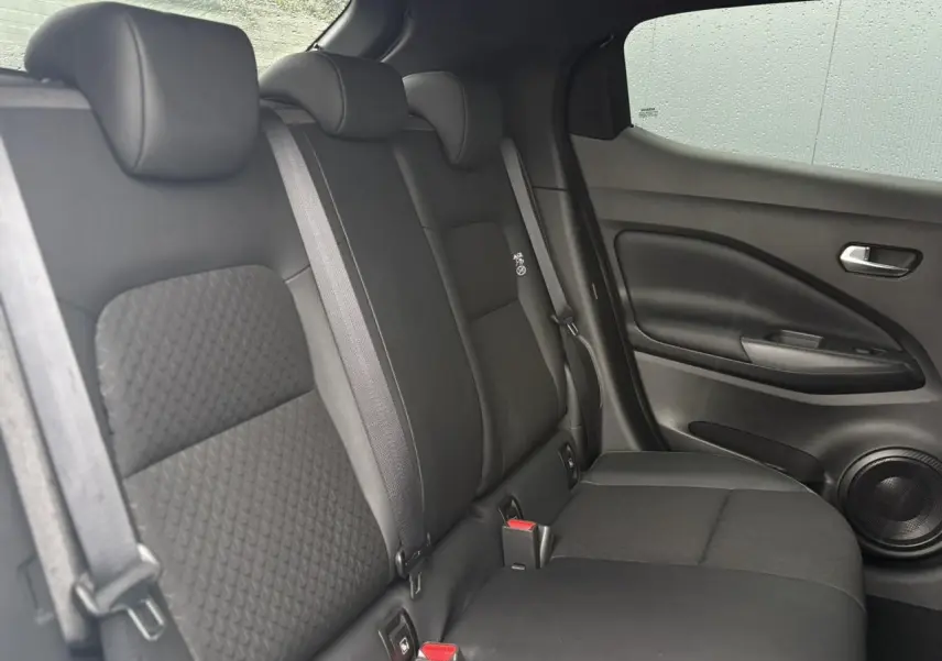 Vue latérale droite de la banquette arrière noire du Nissan Juke 2025 avec ceintures et haut-parleur intégré à la porte.
