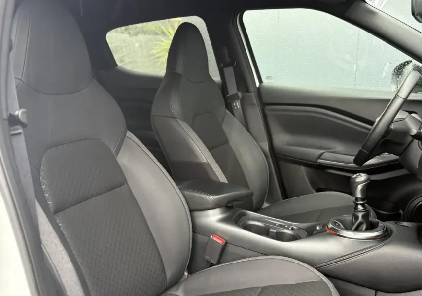 Vue intérieure côté conducteur du Nissan Juke 2025 avec sièges noirs et levier de vitesse manuel visible.