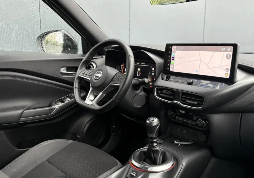 Vue intérieure côté conducteur du Nissan Juke blanc nacré 2025, avec tableau de bord digital et écran tactile GPS.
