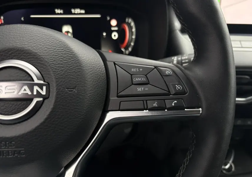 Gros plan sur le volant en cuir noir du Nissan Juke blanc nacré 2025, avec commandes intégrées au côté droit.