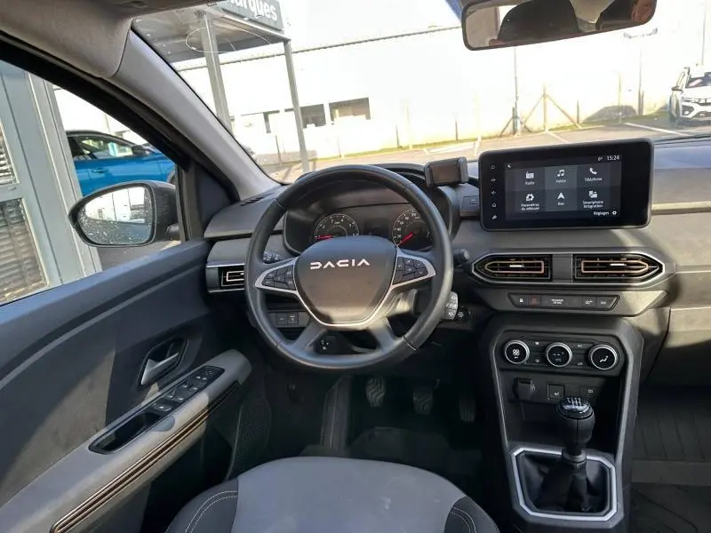 Vue intérieure du poste de conduite de la Dacia Sandero 2025, avec volant multifonction et écran tactile central.