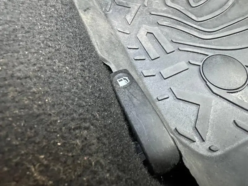 Le levier d'ouverture de trappe à carburant noir sous le tapis de sol intérieur d'une Dacia Sandero 2025.