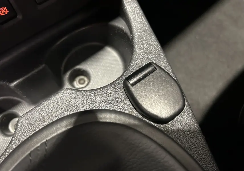 Gros plan sur la console centrale noire du Dacia Duster 2017, mettant en valeur un bouton et un porte-gobelet texturé.