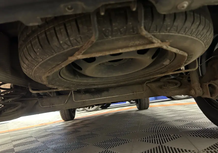 Vue en contre-plongée sous un Dacia Duster gris 2017, montrant la roue de secours sous le coffre et le train arrière.