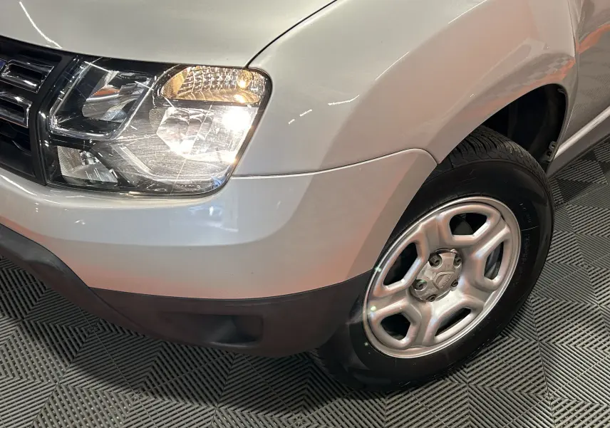 Gros plan sur l'avant droit gris du Dacia Duster 2017, mettant en valeur le phare allumé et la roue en alliage.