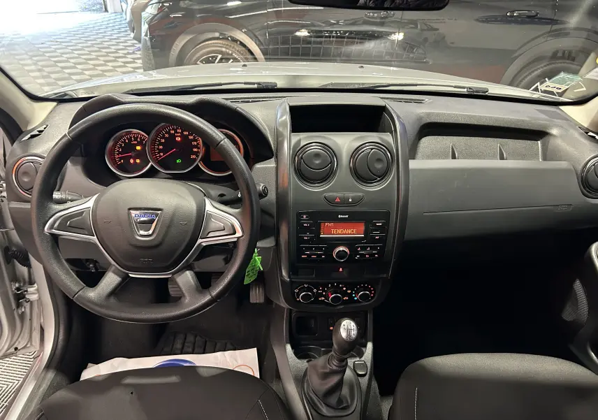 Vue intérieure du tableau de bord et volant noir du Dacia Duster gris 2017 avec console centrale et levier de vitesses manuel.