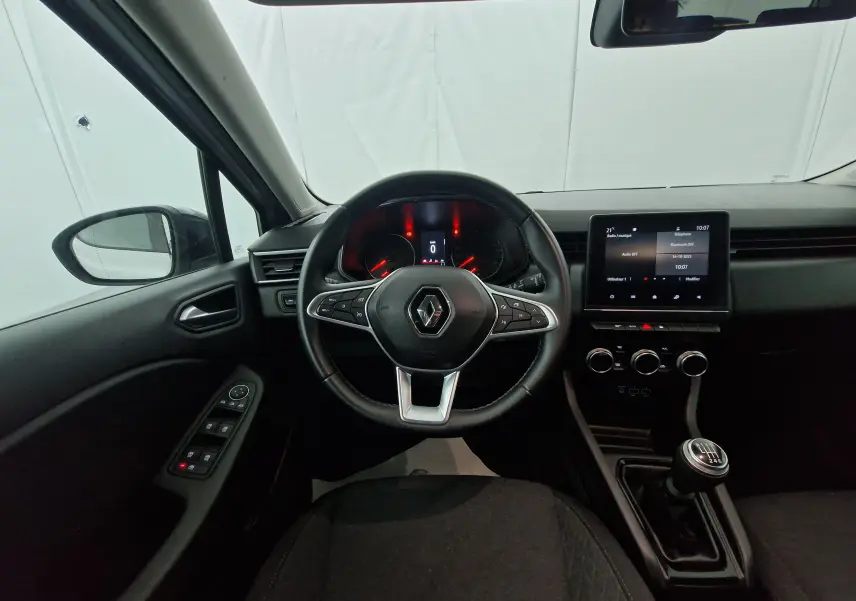 Vue intérieure centrée sur le volant Renault Clio V gris platine, tableau de bord digital et levier de vitesse manuel visible.