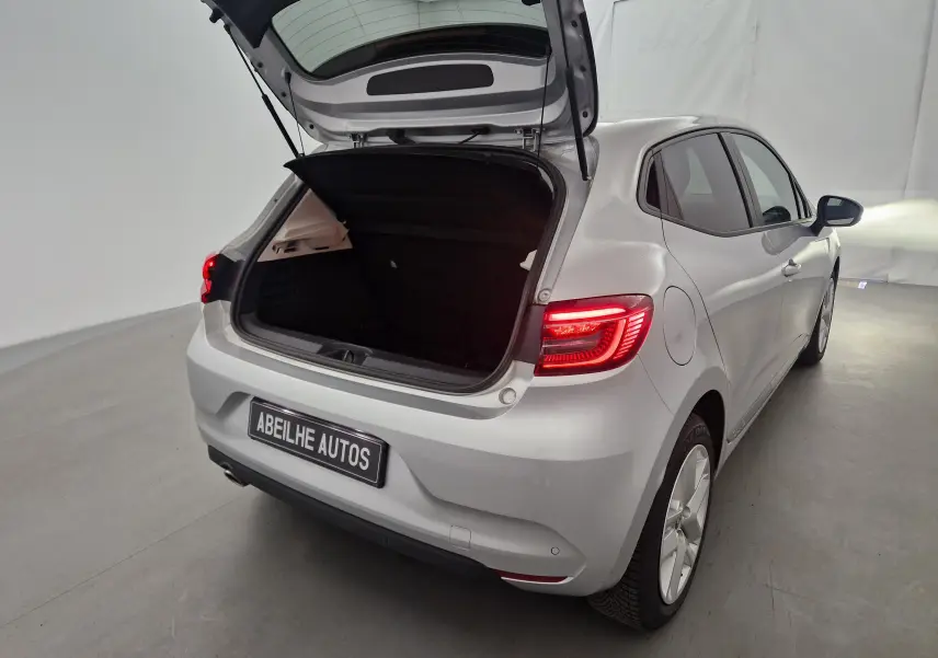 Vue arrière droite d'une Renault Clio V gris platine 2021 avec coffre ouvert et feux arrière allumés.