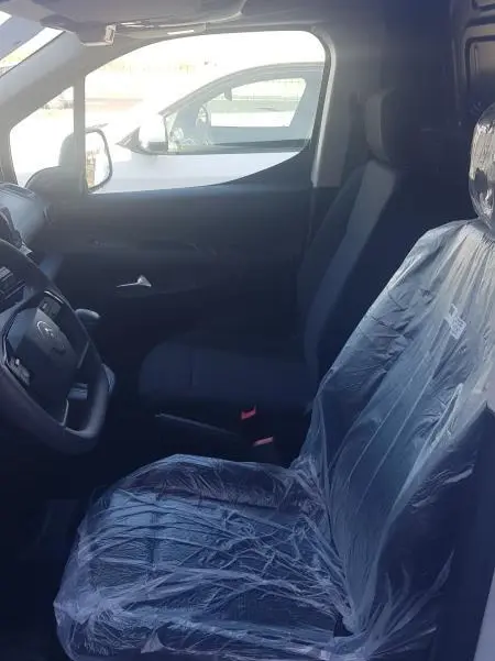 Vue intérieure côté conducteur du Citroën Berlingo blanc 2025, siège protégé par housse plastique, volant multifonctions visible.