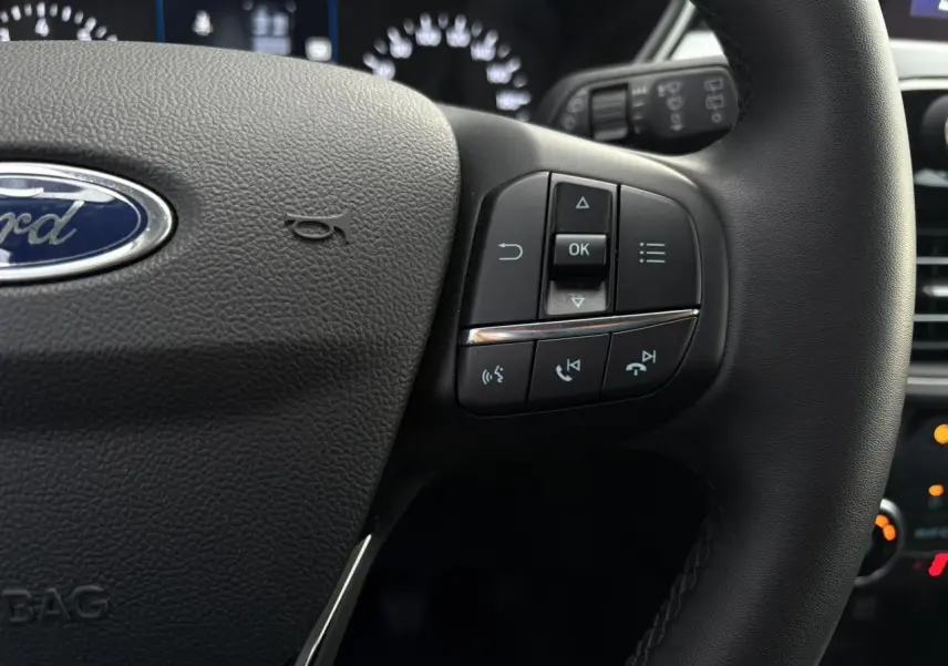 Gros plan sur le volant cuir multifonctions du Ford Kuga 2024, avec commandes intégrées et tableau de bord en arrière-plan.