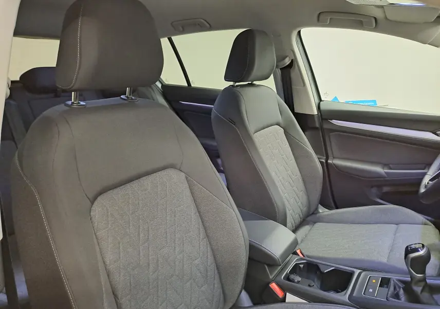 Vue intérieure rapprochée des sièges avant en tissu gris de la Volkswagen Golf 1.5 eTSI 2025, avec levier de vitesses manuel visible.