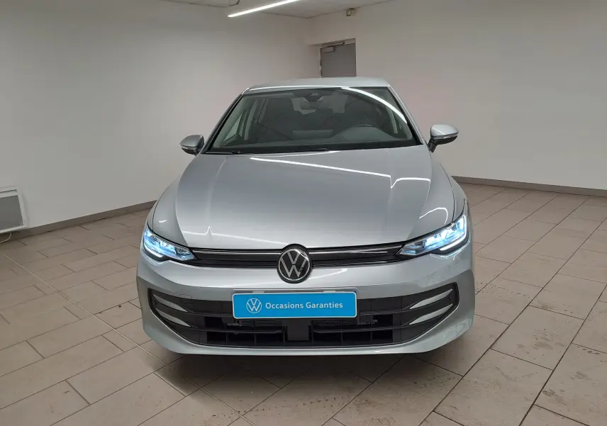 Vue avant d'une Volkswagen Golf 1.5 eTSI 2025 en Argent Dolomite avec phares LED allumés dans un intérieur neutre.