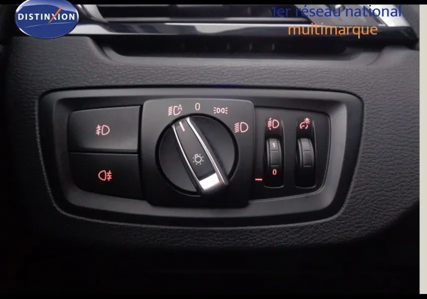 Gros plan sur le panneau de commande des phares du BMW X1 blanc Alpine Metal, avec réglages éclairage et antibrouillard.