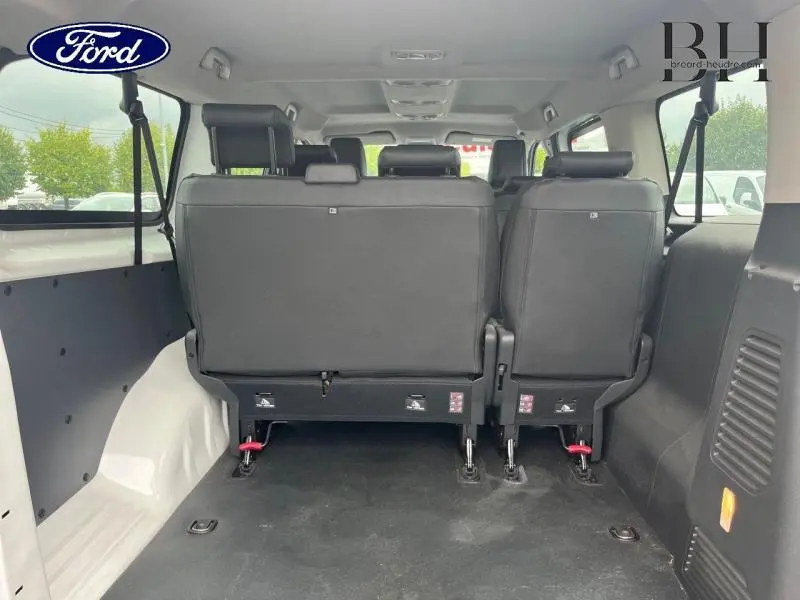 Vue arrière de l'habitacle d'un fourgon blanc avec sièges individuels en deuxième rangée et espace de chargement.